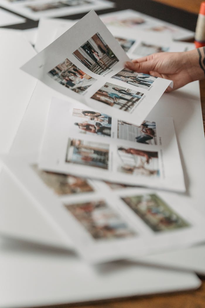 Crop anonymous person looking through printed photos scattered on floor in light room